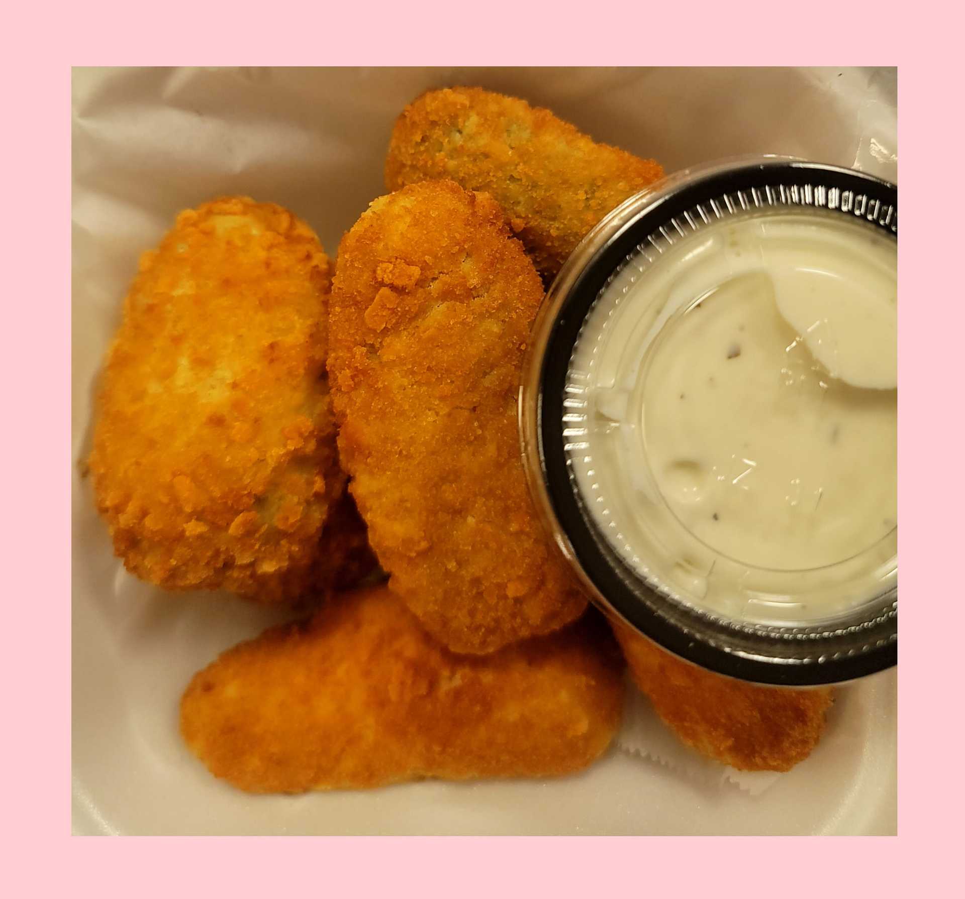 Chicken nuggets and dipping sauce in a takeout container, with a pink border around the image.