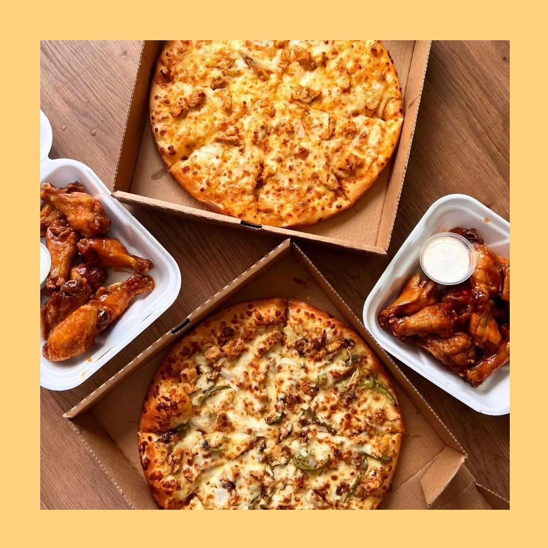 Pizzas and chicken wings in takeout boxes arranged on a wooden table.