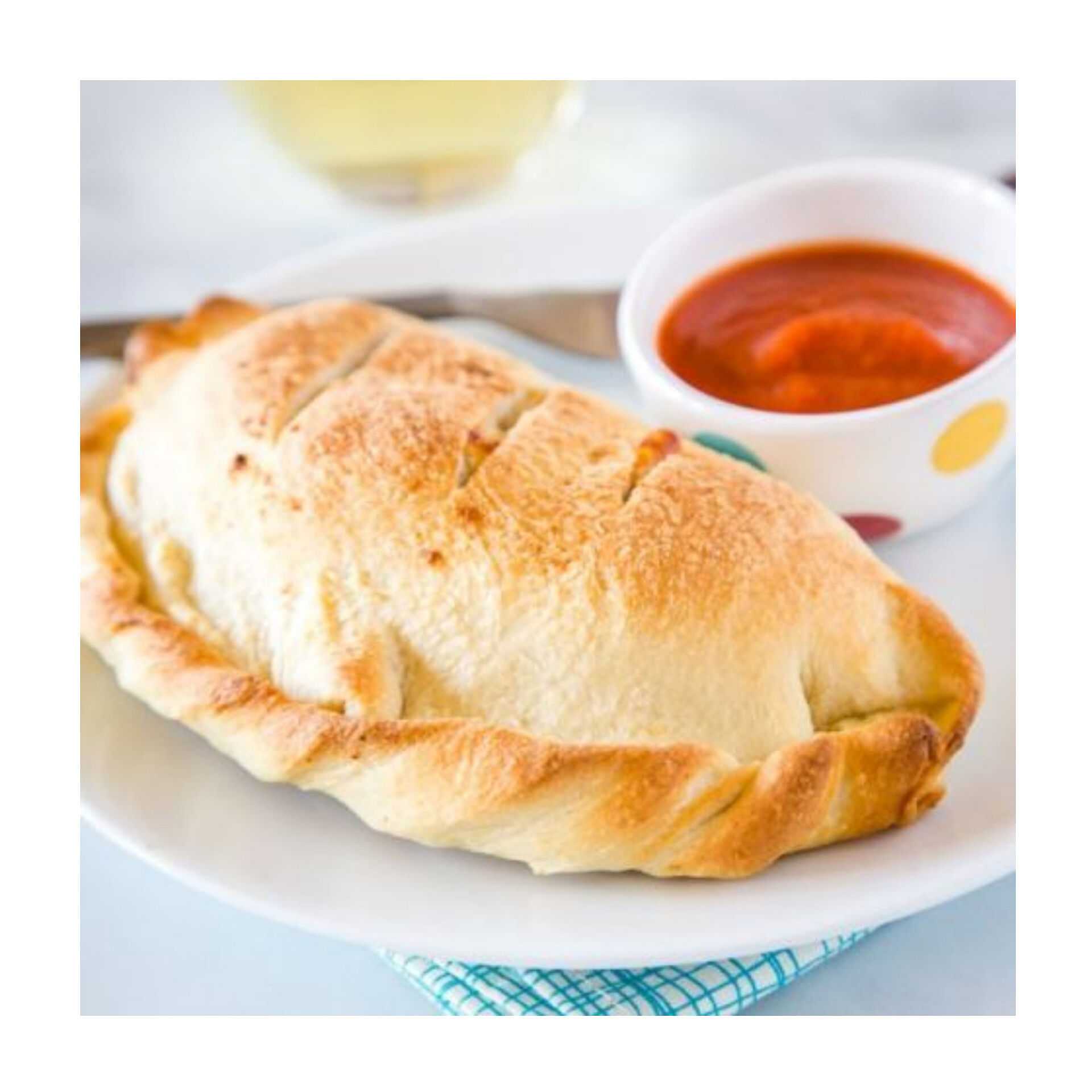 Golden-brown calzone on a white plate, served with a small bowl of marinara sauce.