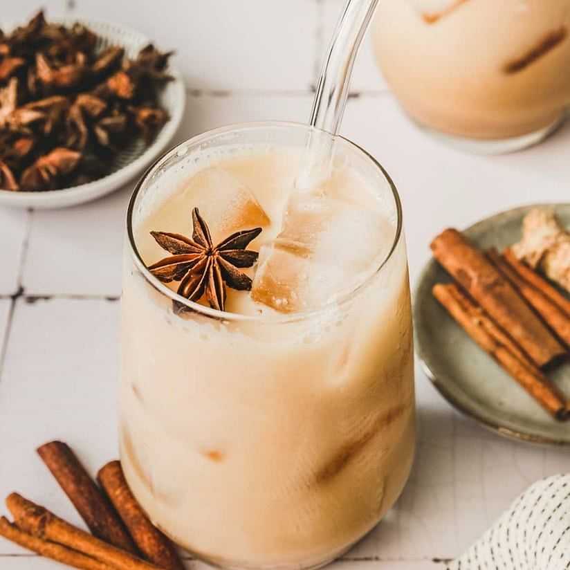 Iced chai latte in a glass with star anise, cinnamon sticks, and a straw.