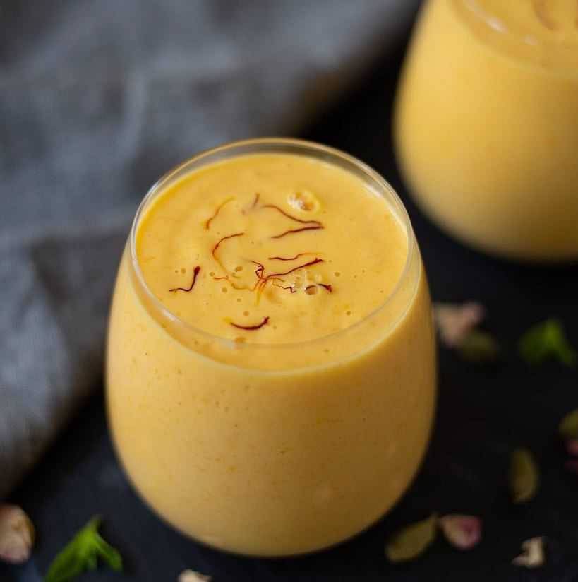 Creamy saffron-flavored smoothie in a glass, garnished with saffron strands, on a dark surface.