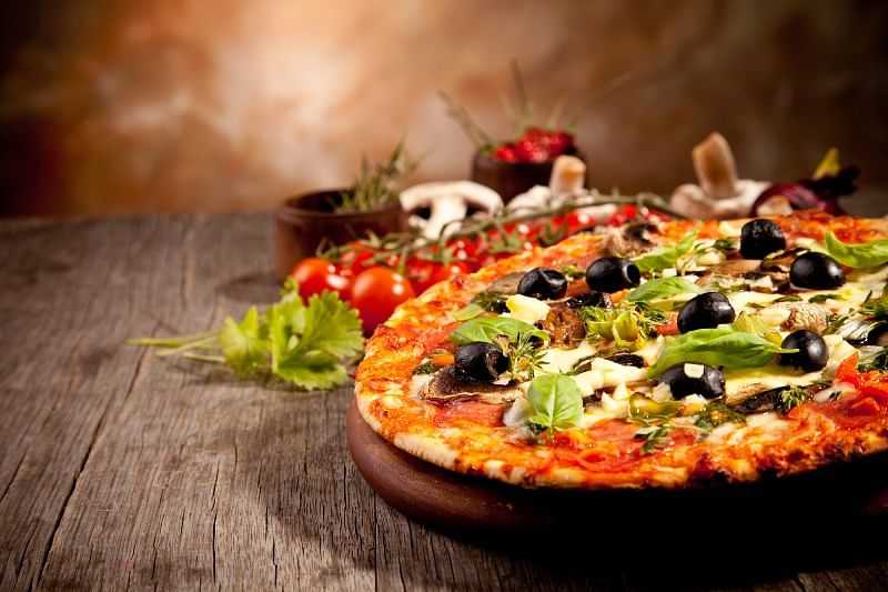 A freshly baked vegetable pizza topped with olives, garlic, and herbs on a rustic wooden table.
